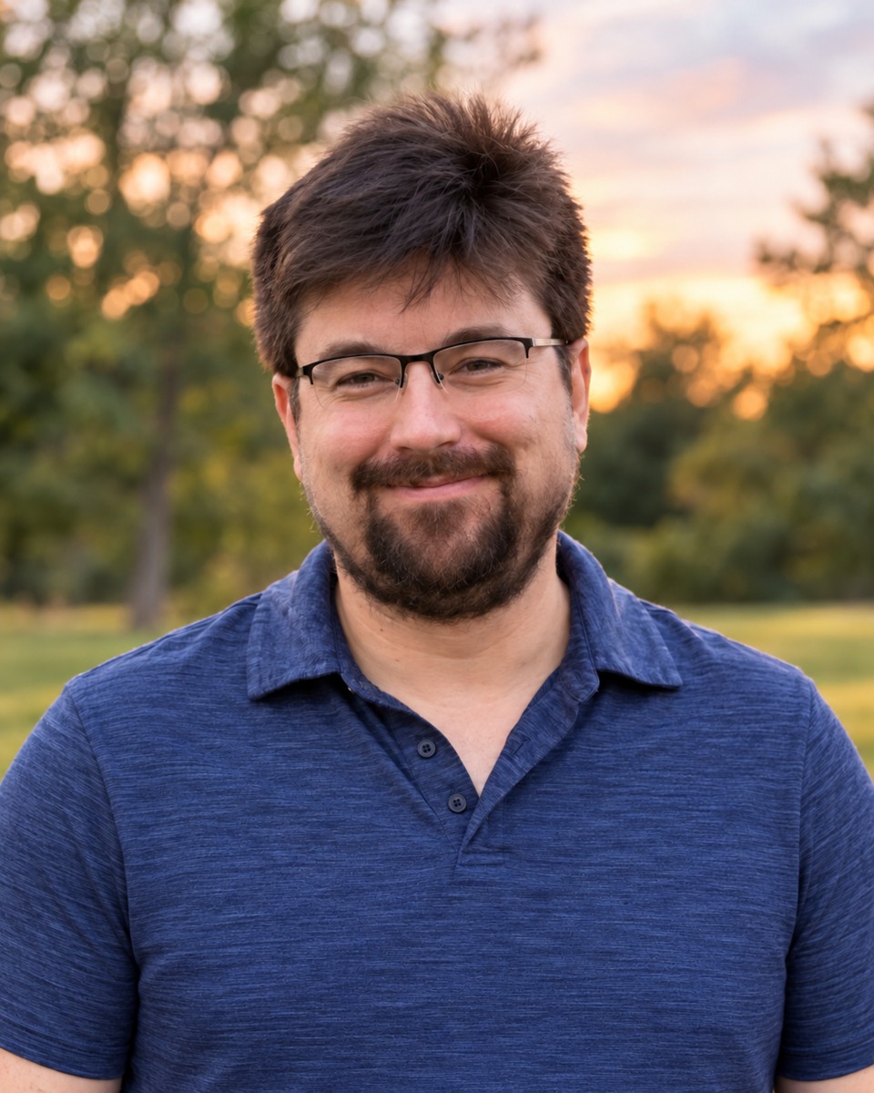 Portrait of Jonathan smiling in a blue polo against a softly blurred outdoor background.